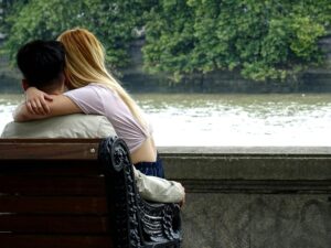 Young couple sharing a tender moment on a park bench by the riverside